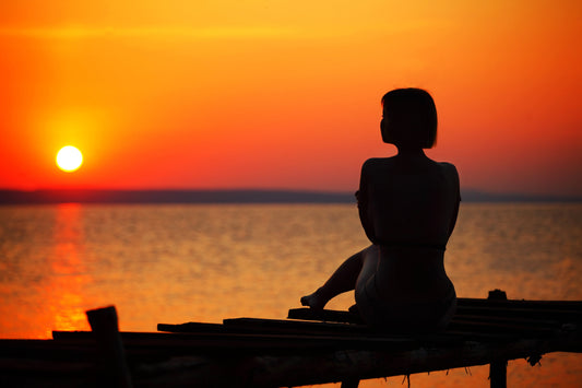 Person sitting alone by the ocean at sunset.