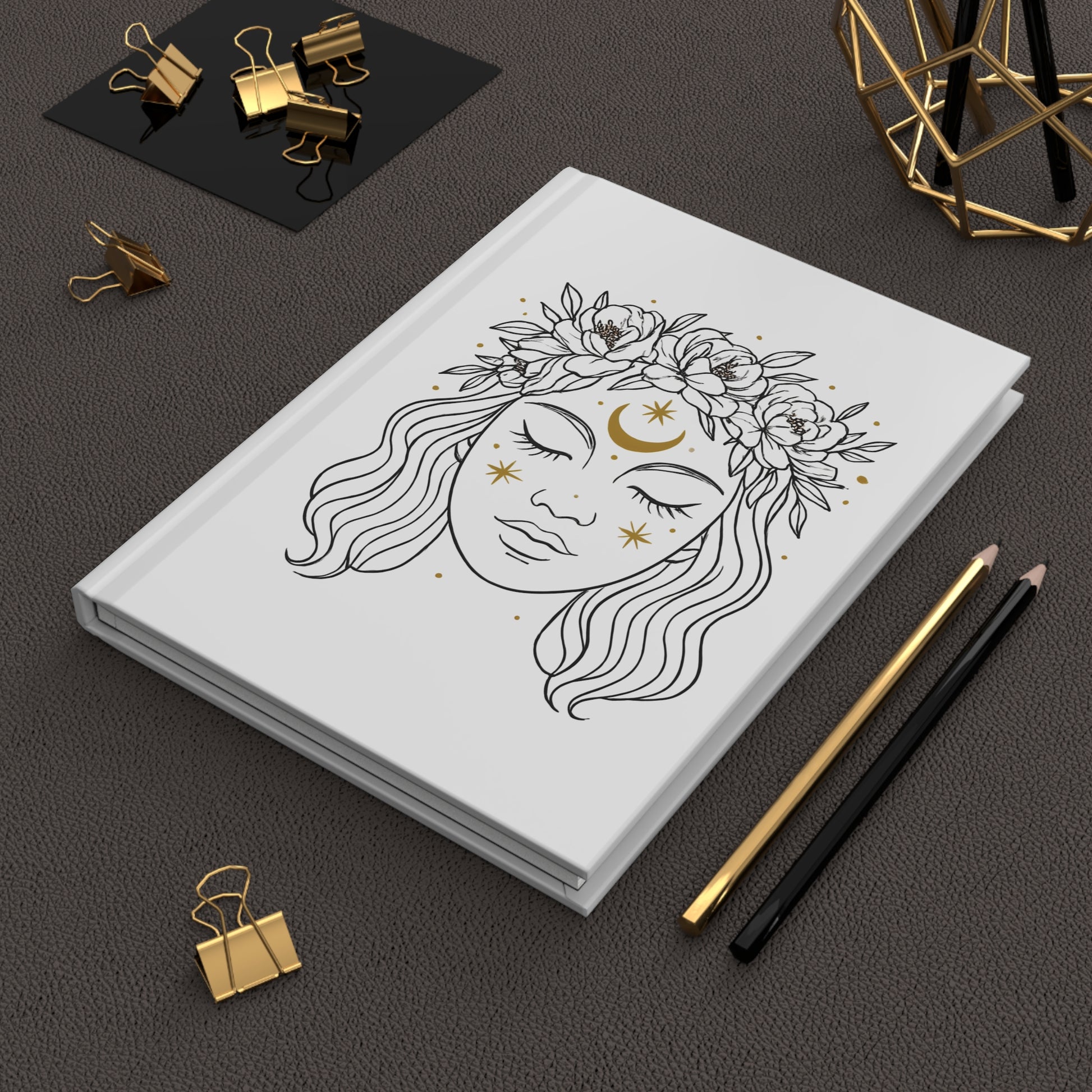 Notebook with artistic cover design on a dark surface with stationery items.