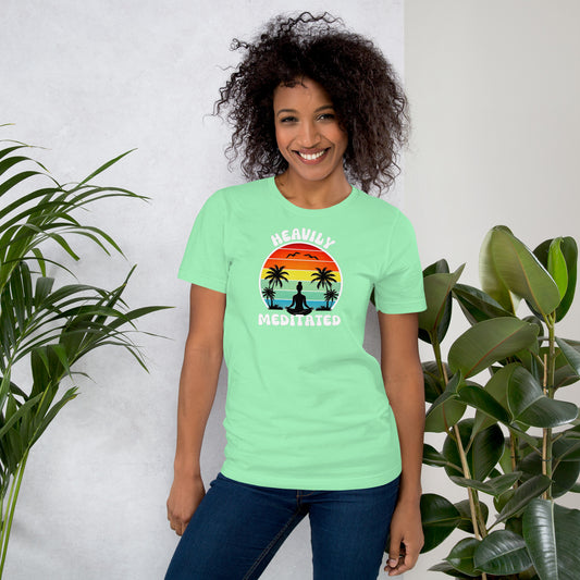 Woman wearing a light green t-shirt with a heavily meditated graphic design and text, standing against a white background with plants.